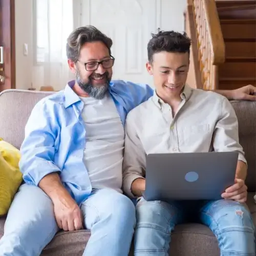 Father and son sitting on couch looking at laptop